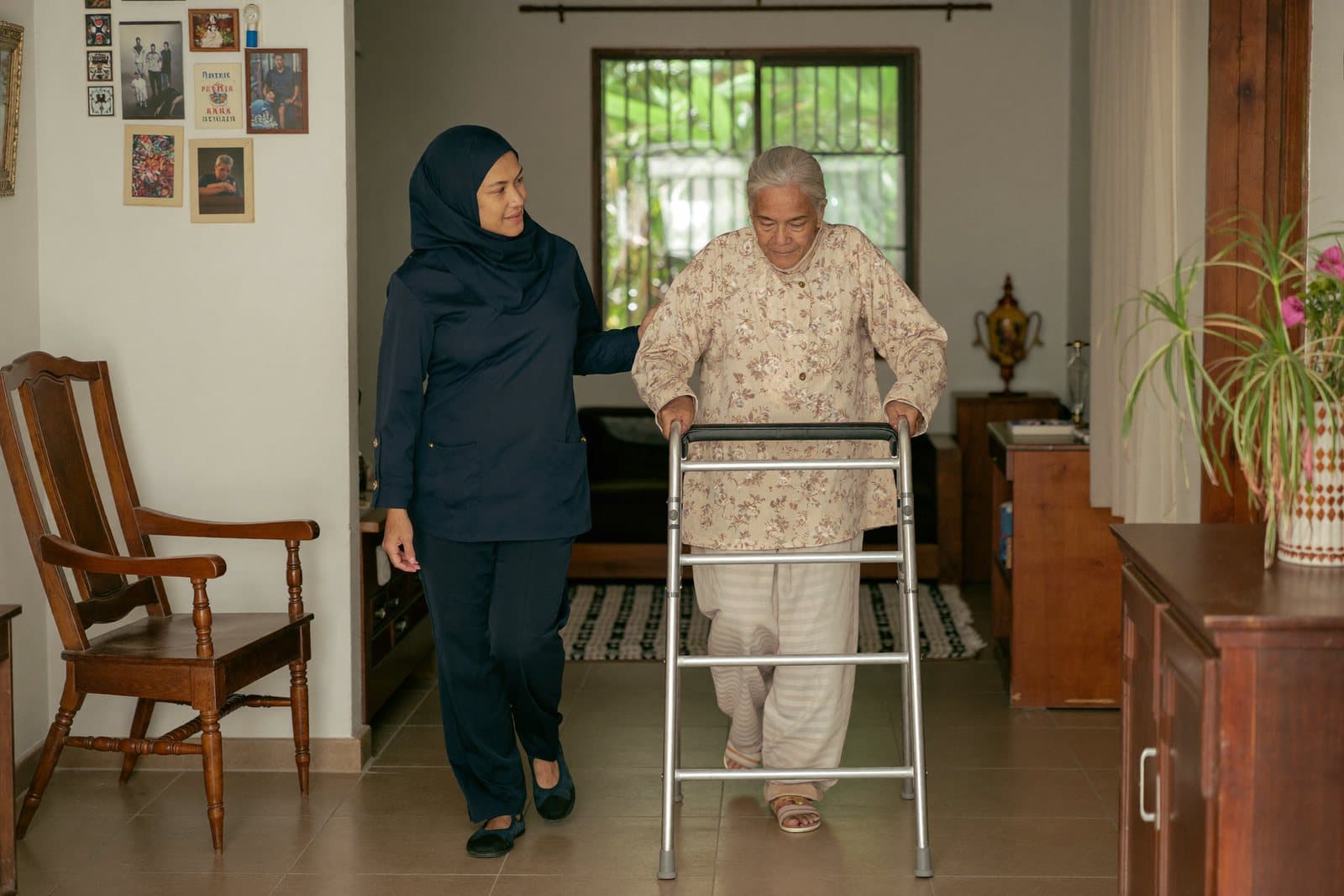 A physiotherapist walking beside an older patient using a walking frame at home