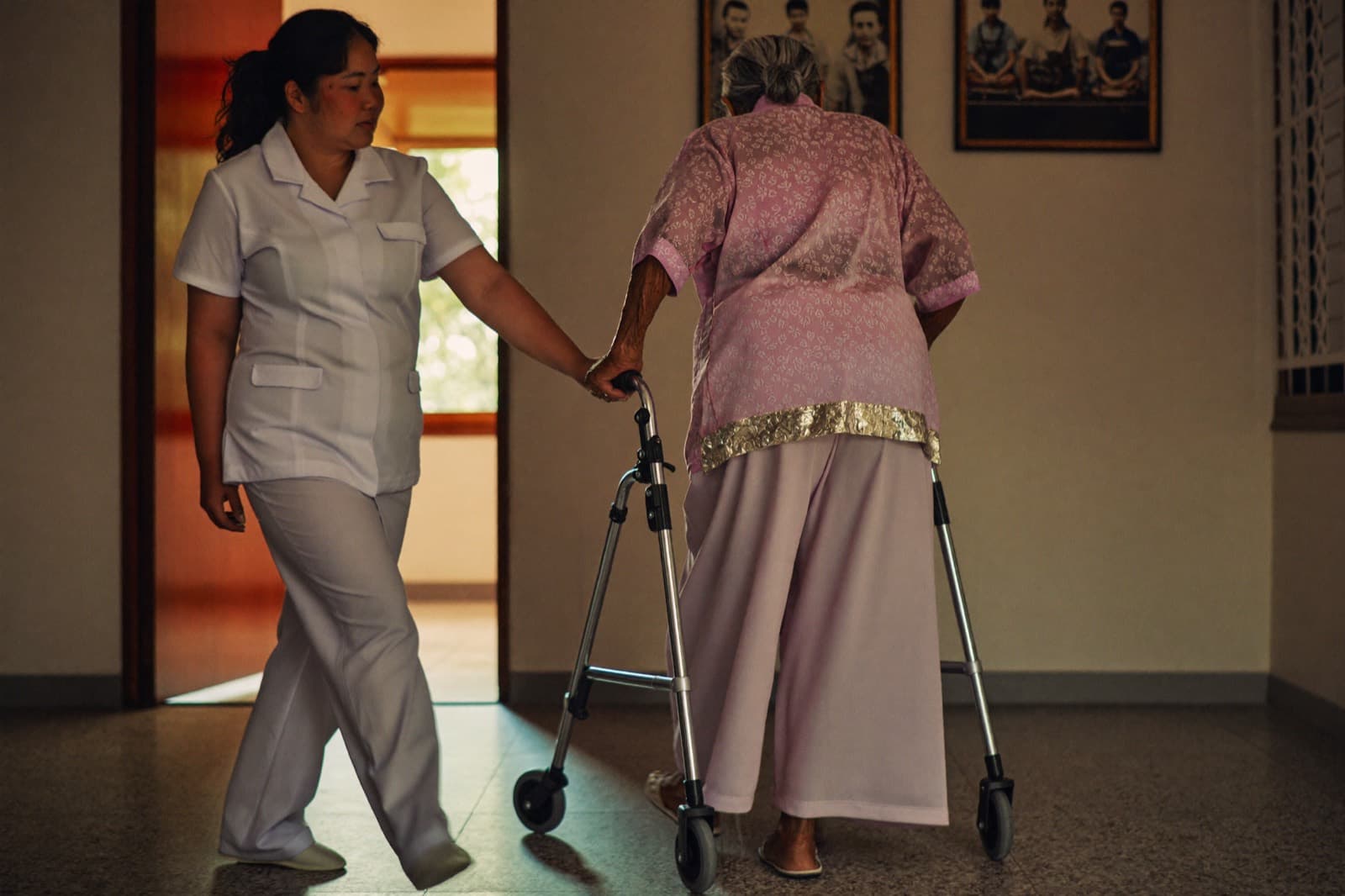 A physiotherapist walking beside an older patient using a walking frame at home