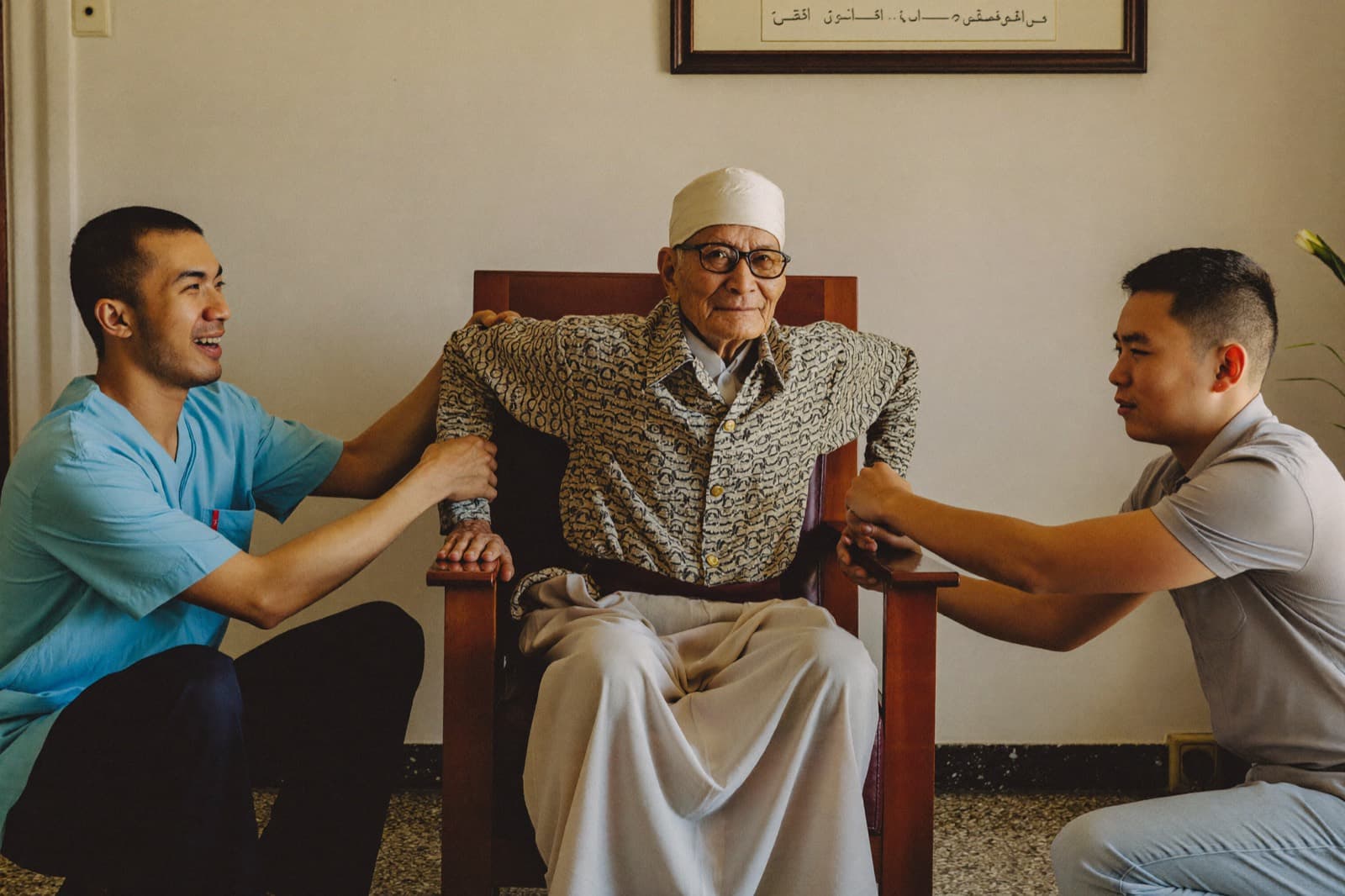 A physiotherapist and a son helping an older man stand up from his armchair