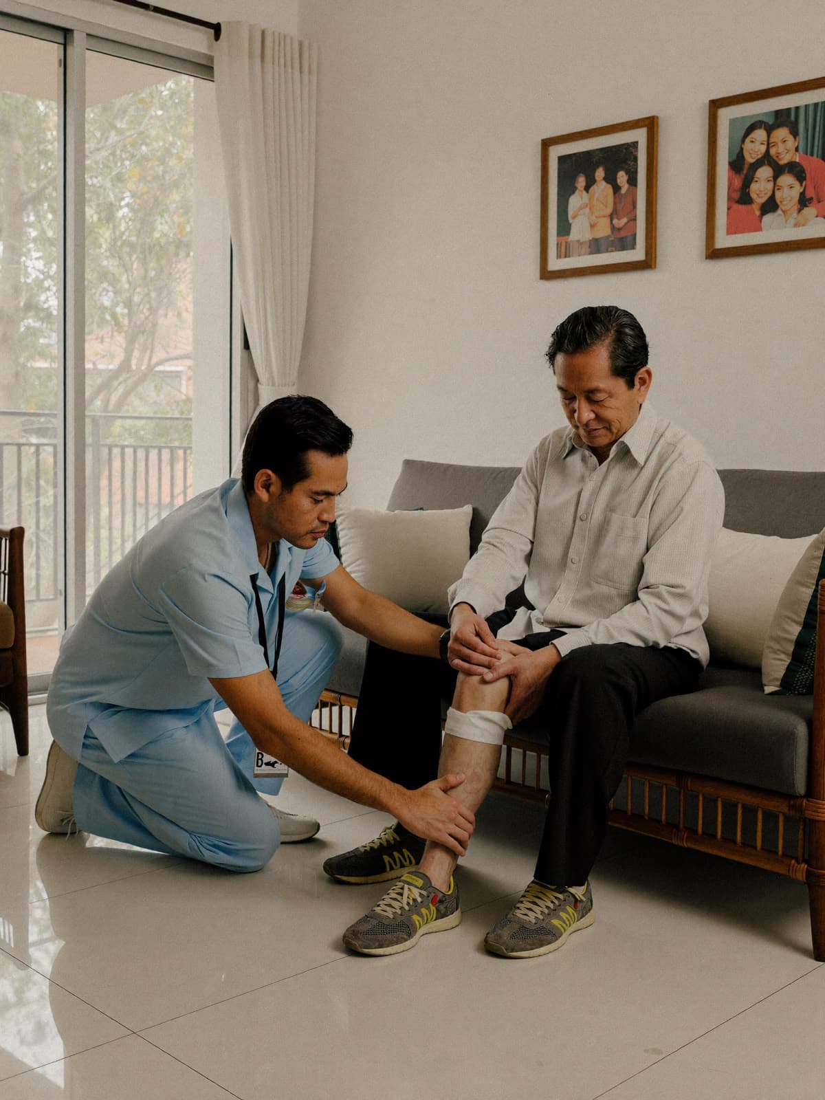 A male physiotherapist guiding an older male patient through a knee exercise in his living room
