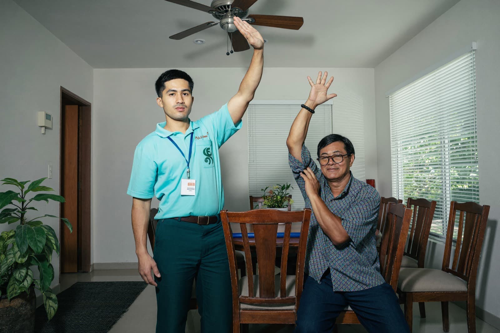 A male physiotherapist demonstrating an arm exercise to an older male patient at home